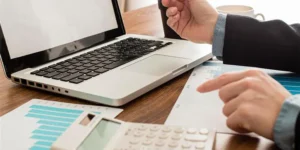 Accountant reviewing financial reports on a laptop and calculator for a blog about what is included in bookkeeping services.