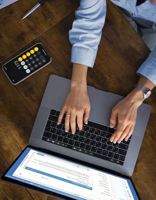 High-angle view of a professional typing on a laptop with a calculator app nearby, representing the data-driven efficiency of startups receivable services.