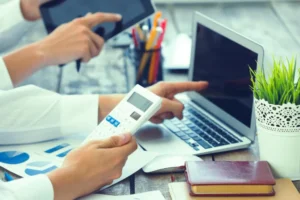 A business professional pointing at a laptop screen and holding a calculator, demonstrating why outsource accounting services help with financial data analysis.