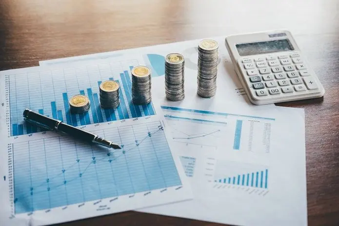 A calculator, pen, and financial charts used for measuring growth and calculating essential ecommerce KPIs.