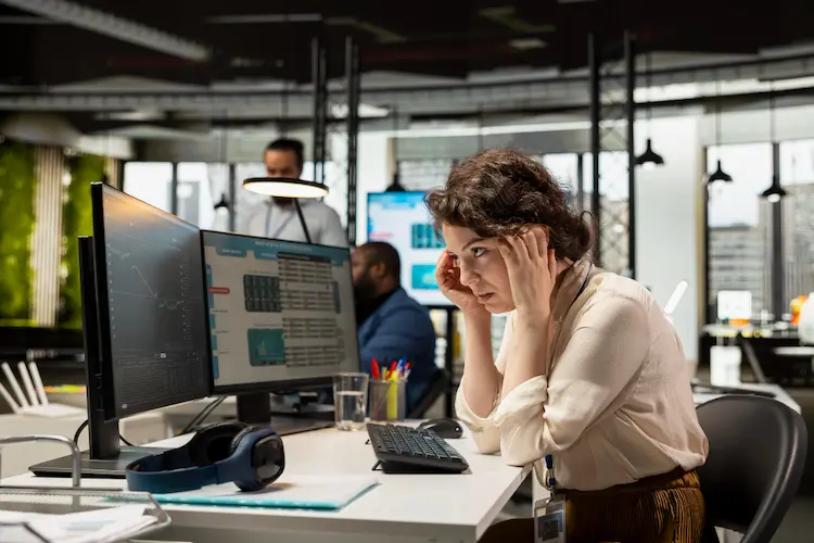 An office professional looking intently at computer screens while navigating a high volume of ecommerce KPIs and performance metrics.