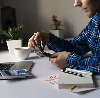 A business owner counting currency and reviewing expenses, illustrating the daily cash flow challenges solved by payable for startups.