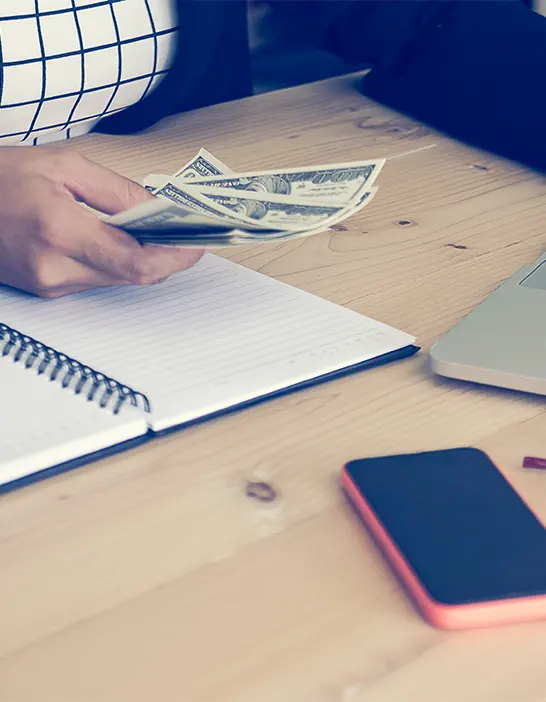 Close-up of a professional holding cash over a ledger, highlighting the importance of organized and secure payable services for startups.