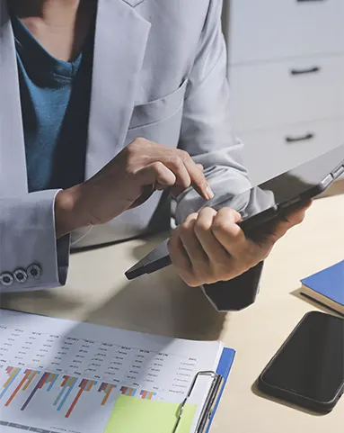 A financial expert using a tablet to track data and manage payable services for startups alongside printed performance charts.