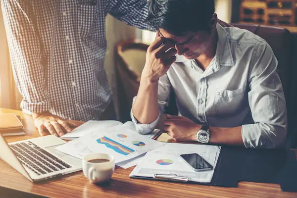 Stressed professional analyzing complex financial reports, highlighting the benefits of outsourcing bookkeeping to improve business focus and accuracy.