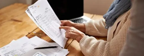 Person reviewing financial documents and invoices at a desk with a laptop.