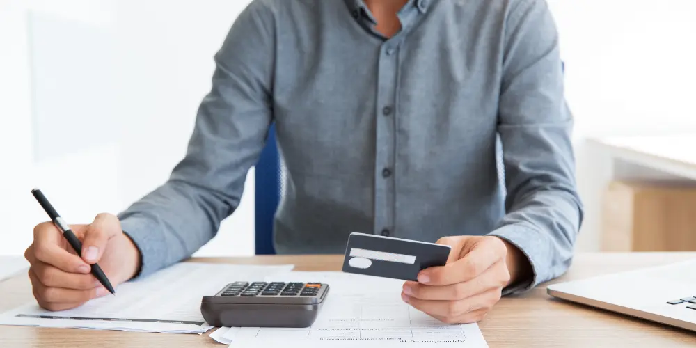 Person calculating expenses with a calculator, documents, and credit card